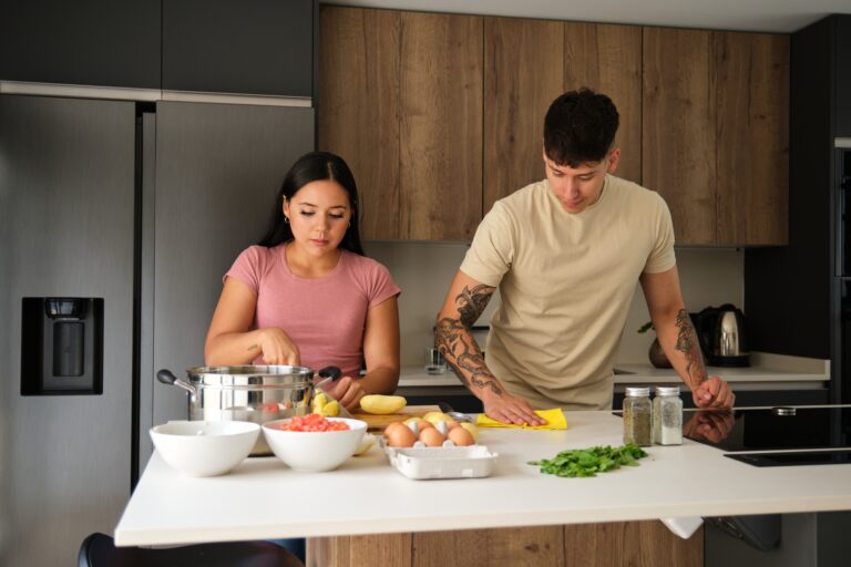 Two young latin people peeling potatoes and cleaning kitchen counter at kitchen.