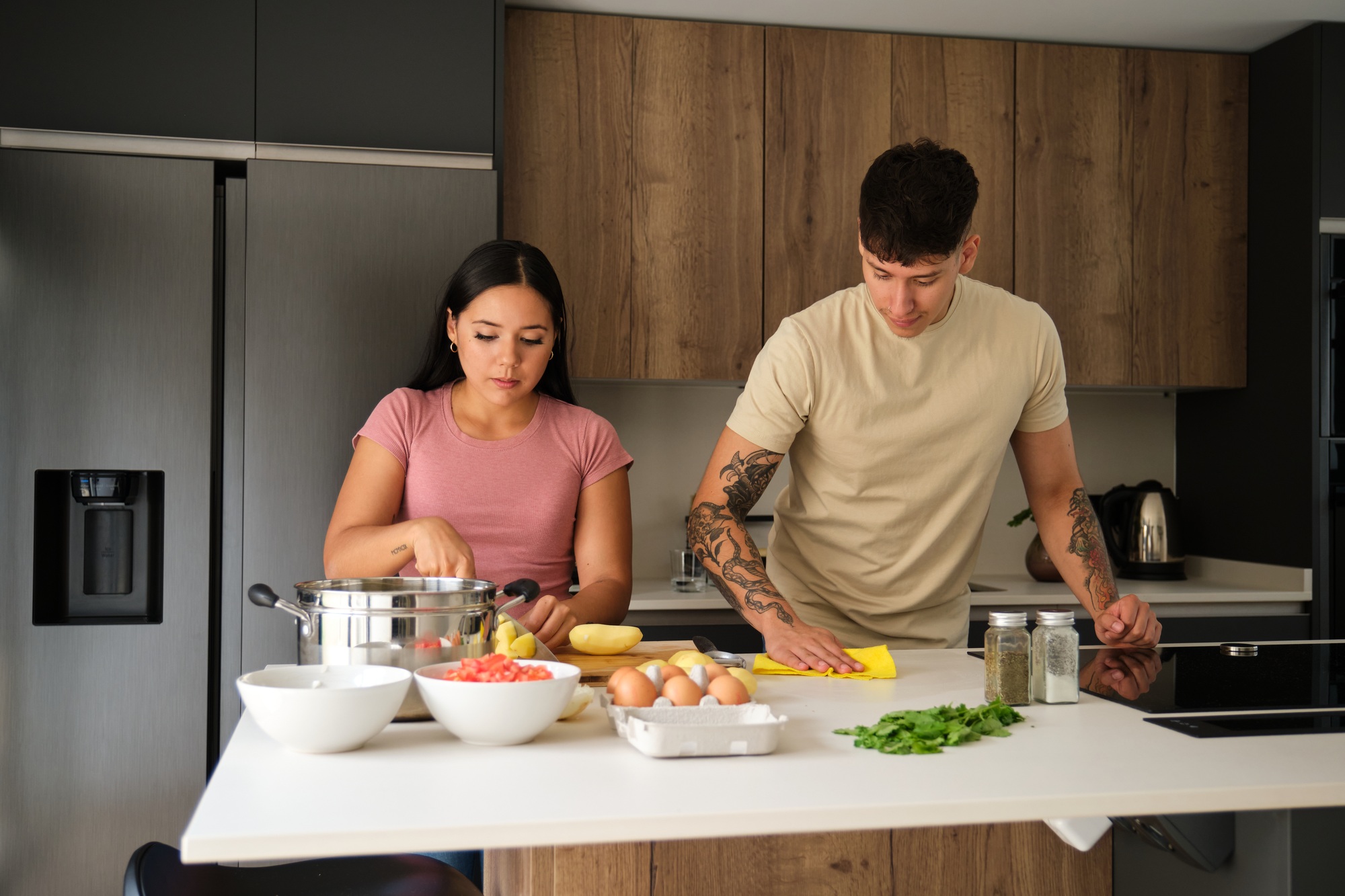 Two young latin people peeling potatoes and cleaning kitchen counter at kitchen.